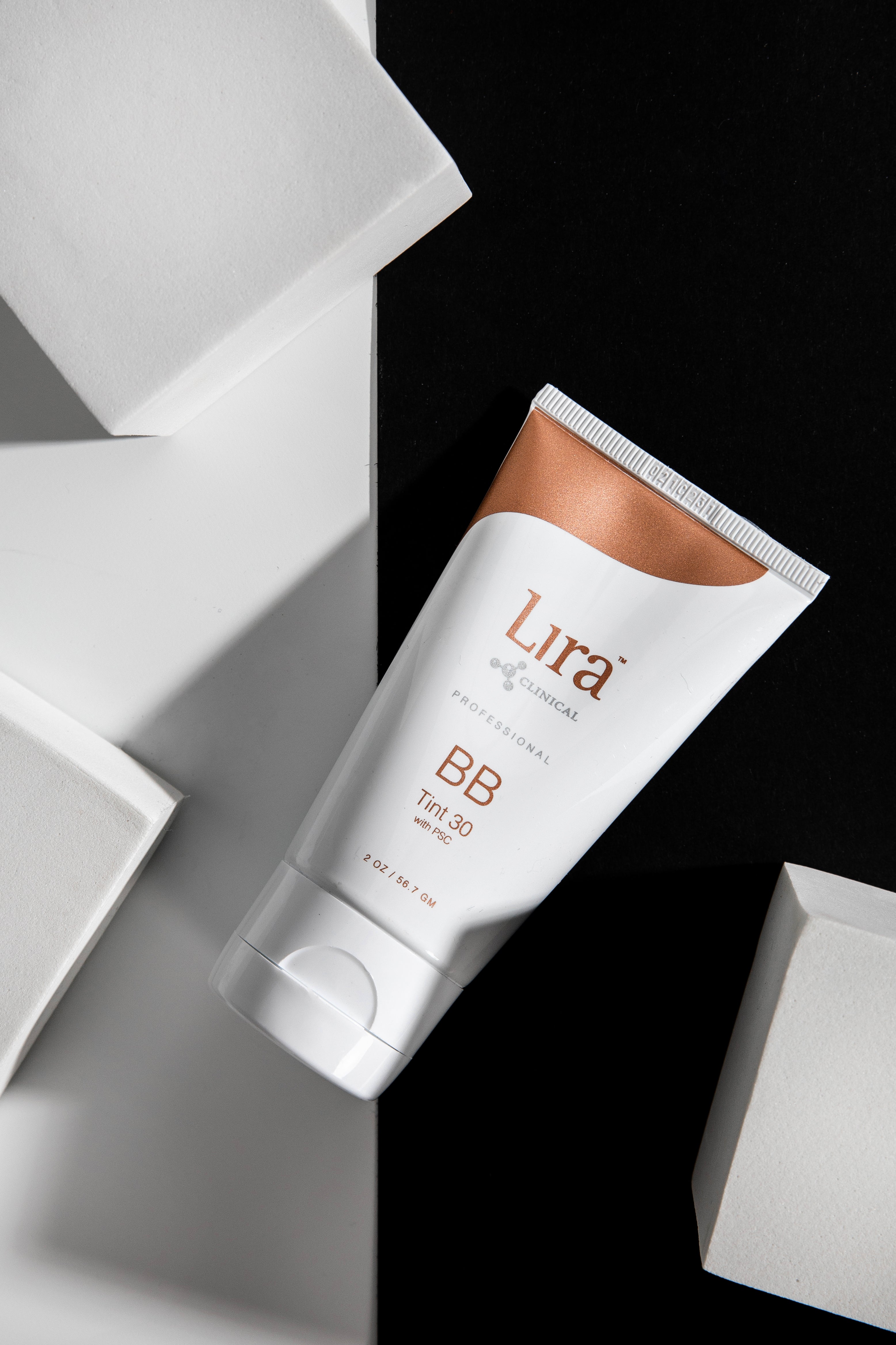 Lira Clinical BB Tint 30 cream, placed on a black background along with white boxes lying around