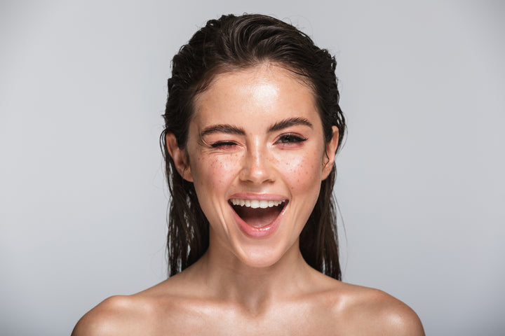 A beautiful young girl with flawless freckled skin and black hair, winking at your while smiling widely