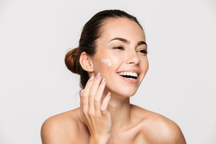 A beautiful girl with flawless skin and perfectly manicured hands, happily applying cream on face 